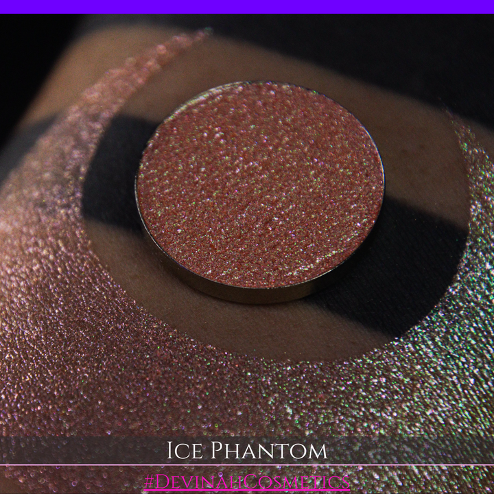 A circular makeup eyeshadow pan of a shimmery rose gold peachy coral eyeshadow labeled 'ICE PHANTOM' by Devinah Cosmetics, shown next to a large swatch on skin.