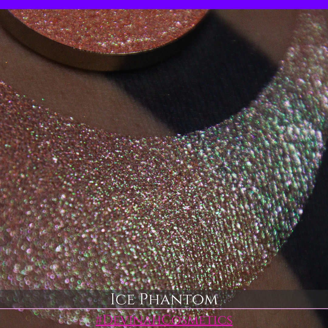 A circular makeup eyeshadow pan of a shimmery rose gold peachy coral eyeshadow labeled 'ICE PHANTOM' by Devinah Cosmetics, shown next to a large swatch on skin.