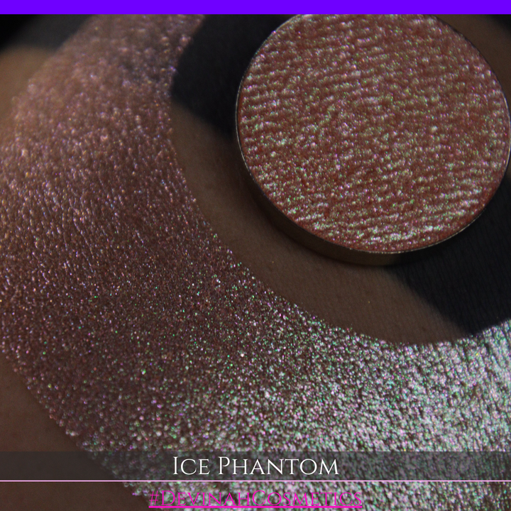 A circular makeup eyeshadow pan of a shimmery rose gold peachy coral eyeshadow labeled 'ICE PHANTOM' by Devinah Cosmetics, shown next to a large swatch on skin.