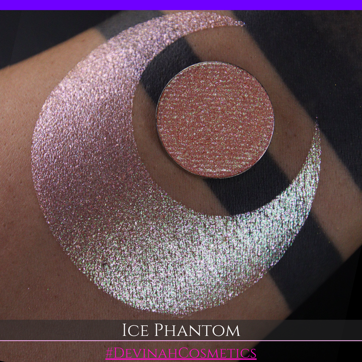 A circular makeup eyeshadow pan of a shimmery rose gold peachy coral eyeshadow labeled 'ICE PHANTOM' by Devinah Cosmetics, shown next to a large swatch on skin.