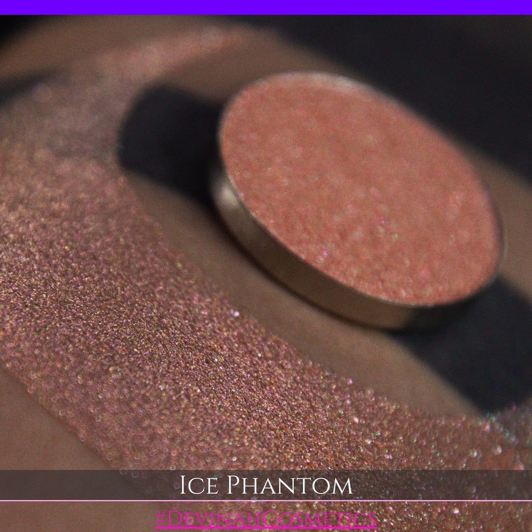 A circular makeup eyeshadow pan of a shimmery rose gold peachy coral eyeshadow labeled 'ICE PHANTOM' by Devinah Cosmetics, shown next to a large swatch on skin.
