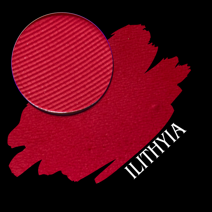A circular makeup eyeshadow pan of vibrant berry red eyeshadow shown over a matching textured red swatch on a black background, with the shade name 'ILITHYIA' in white text.