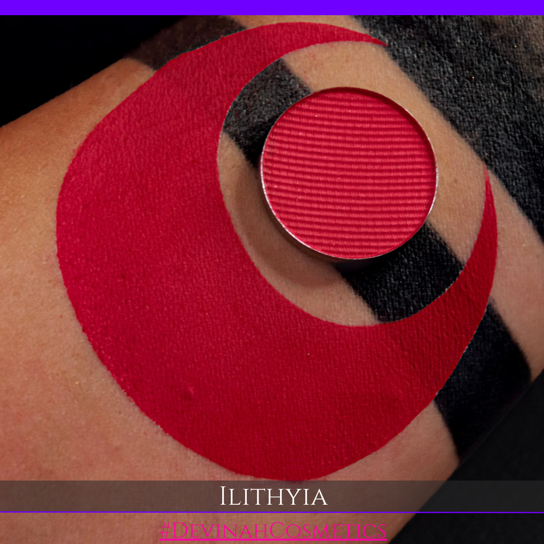 A close-up of a person's skin with a large red crescent-shaped makeup smear and a circular red pressed powder pan placed on top. The brand name ILITHYIA is visible in text at the bottom.