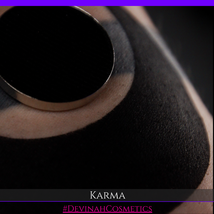 Close-up of a black makeup sponge or applicator pad with a circular metal rim, resting on skin. Text at the bottom reads 'KARMA' and '#DEVINAHCOSMETICS'.