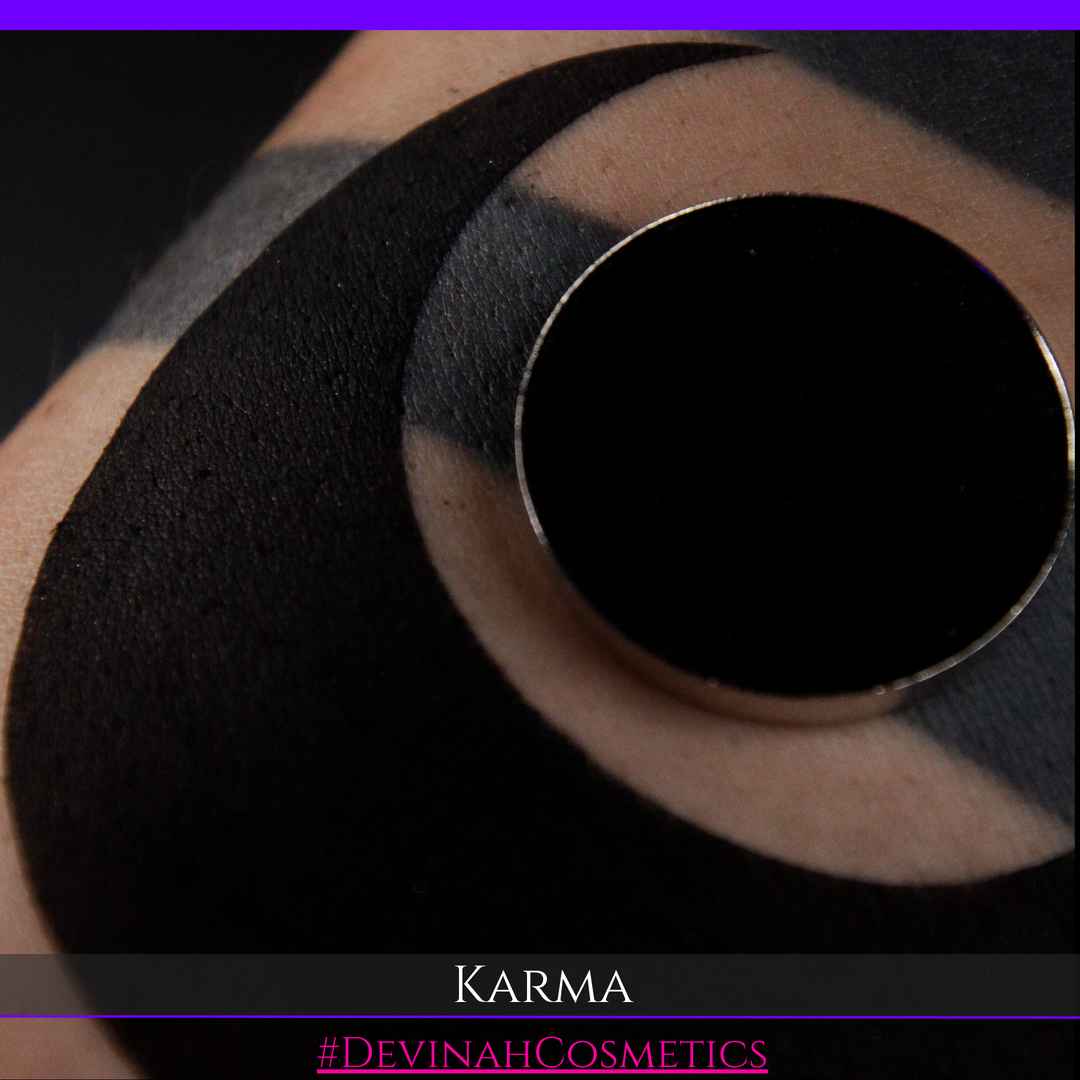 A close-up of a person's skin with a black circular tattoo or body art design, featuring a metallic ring detail and the text 'KARMA' and '#DEVINAHCOSMETICS' at the bottom.