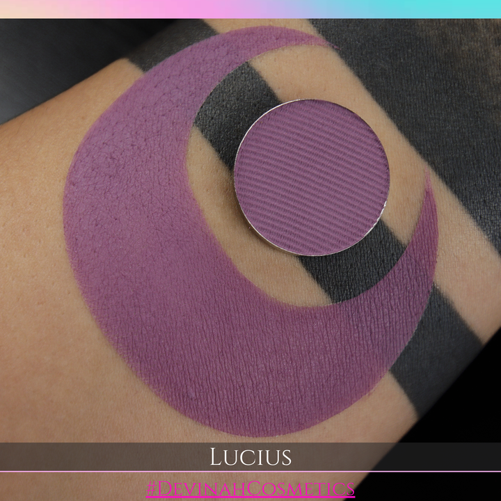 Purple makeup swatch on skin with 'Lucius' brand name at the bottom.