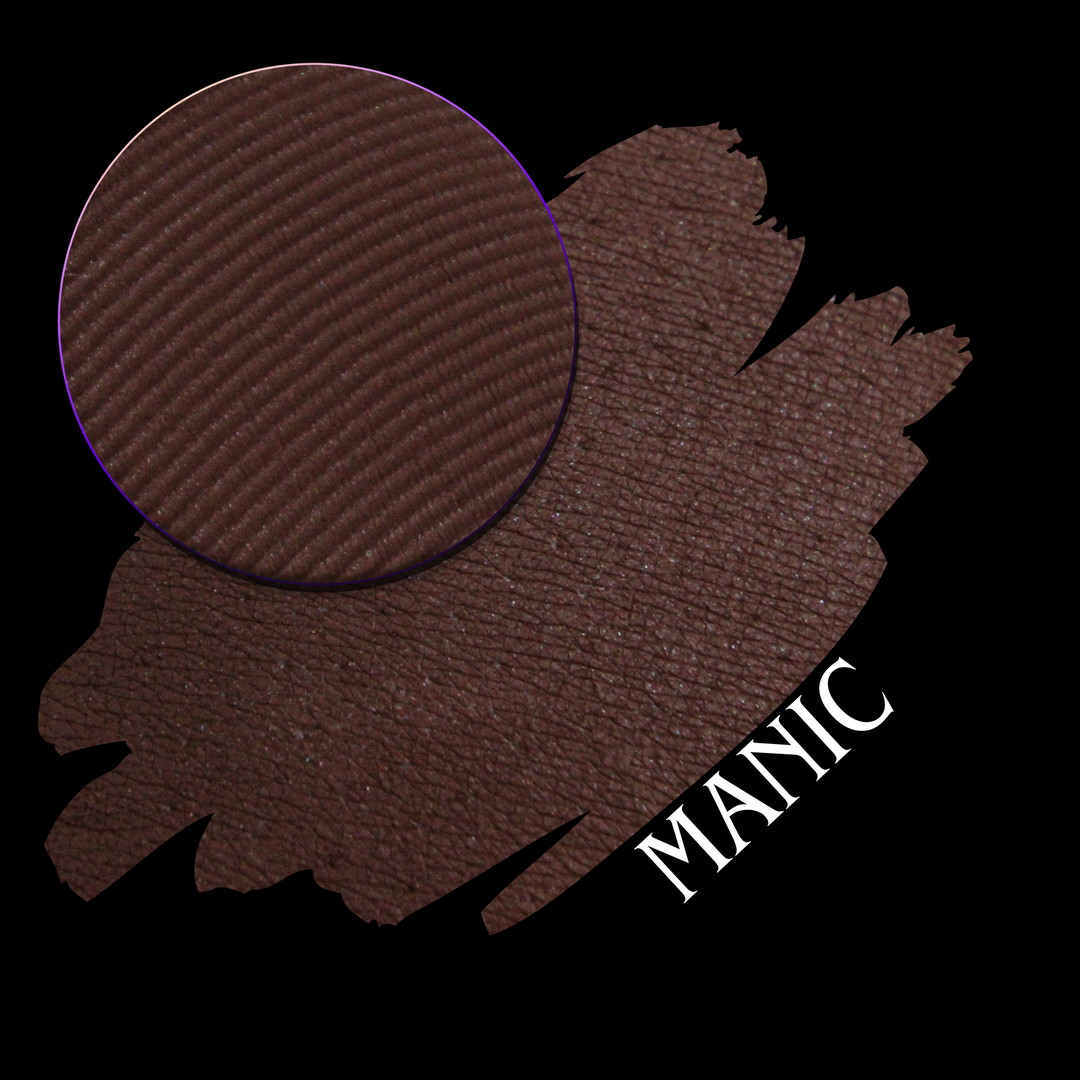 An eyeshadow swatch in a dark brown shade with a circular eyeshadow makeup pan and the word 'MANIC' written in white on a black background.