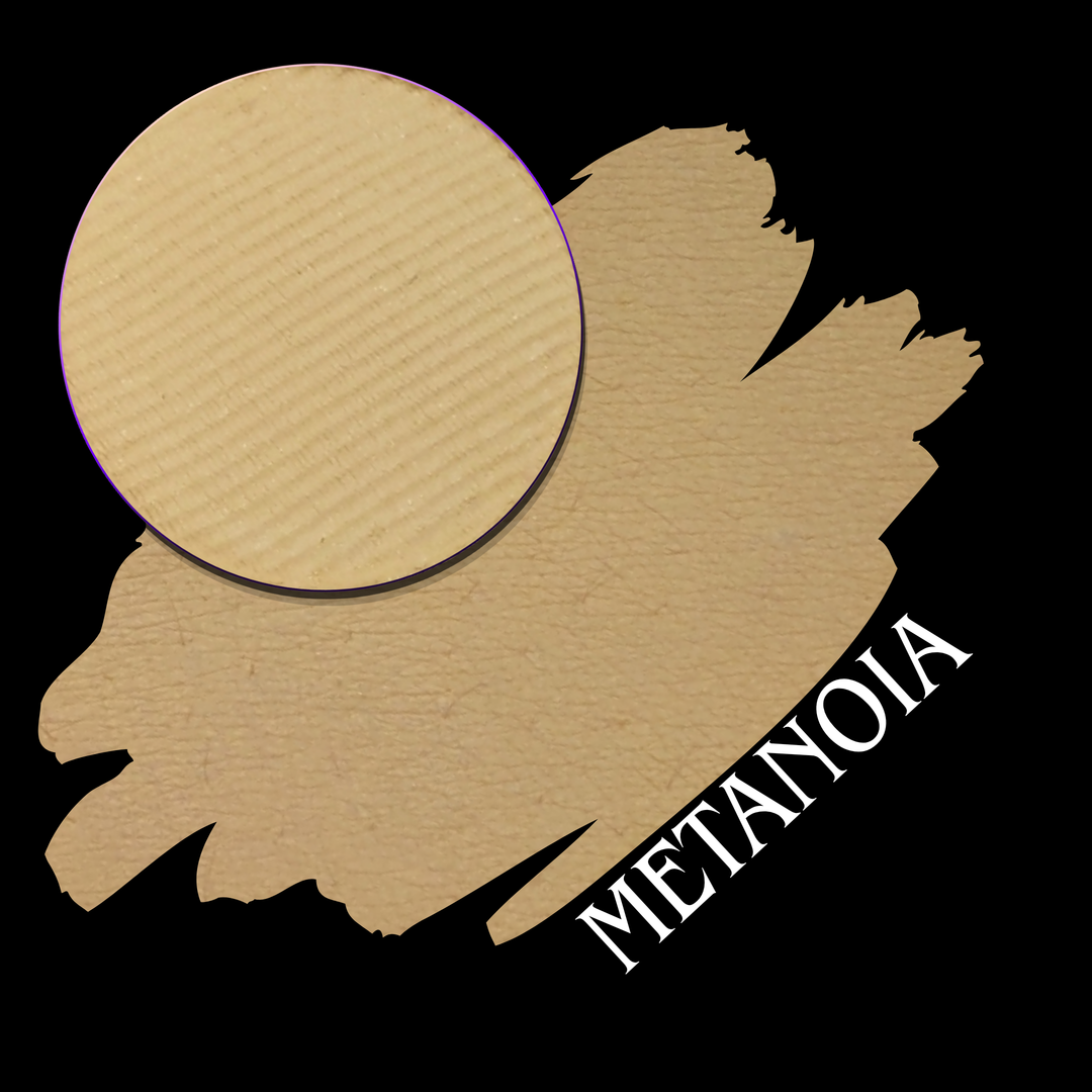 Swatch of a beige eyeshadow with a circular makeup pan, overlaid on a black background with the word 'METANOIA' in white text.