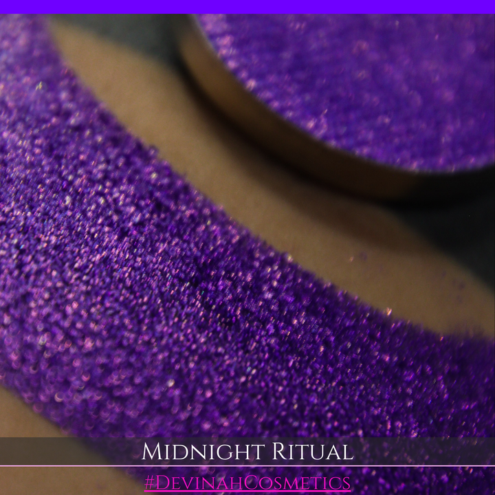 A close-up of a large glittery purple makeup swatch and a matching round pan of purple eyeshadow. Text at the bottom reads 'MIDNIGHT RITUAL' and '#DEVINAHCOSMETICS'.