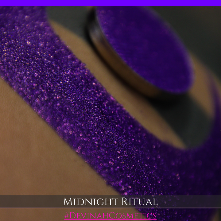 A close-up of a large glittery purple makeup swatch and a matching round pan of purple eyeshadow. Text at the bottom reads 'MIDNIGHT RITUAL' and '#DEVINAHCOSMETICS'.