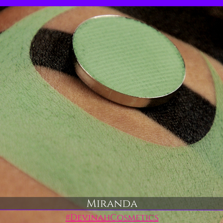 A close-up of a textured light green cosmetic product, likely a cream or powder makeup pan, resting on a beige and black patterned surface. The text 'MIRANDA' are displayed at the bottom.