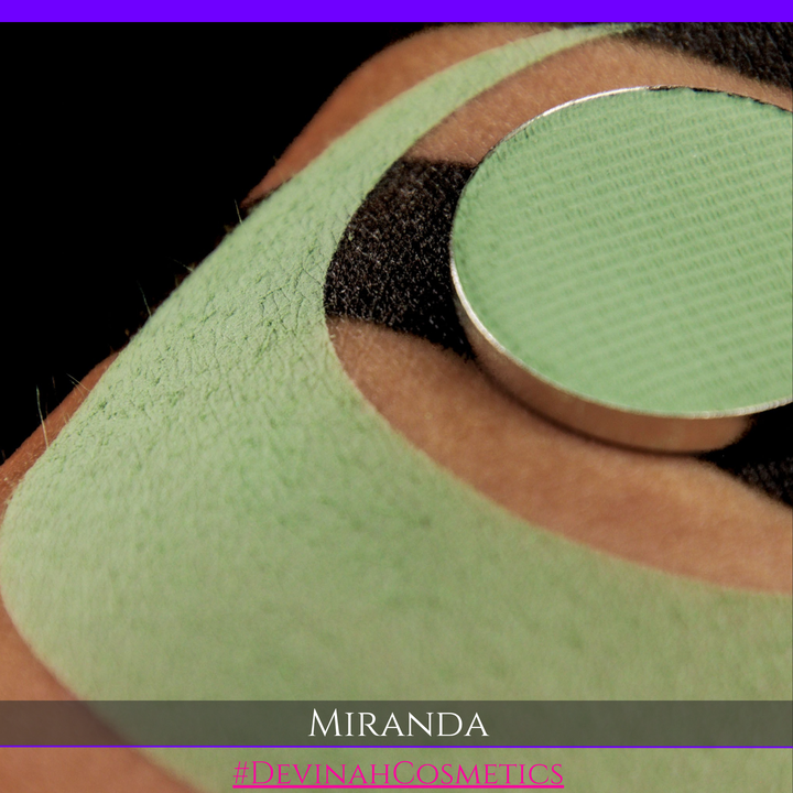 A close-up of a person's eyebrow area showing a light green eyebrow pencil or makeup pan applied, with a green eyebrow patch or stencil underneath. The text overlay at the bottom reads 'MIRANDA' and '#DEVINAHCOSMETICS'.