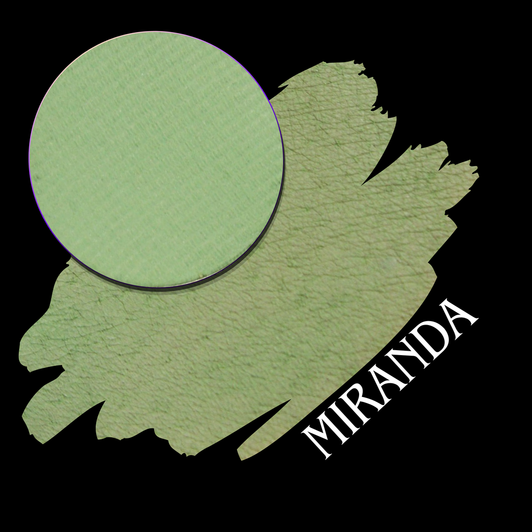 A circular eyeshadow pan of light sage green layered over a larger eyeshadow swatch in the same color, with the name 'MIRANDA' printed in white along the lower right edge on a black background.