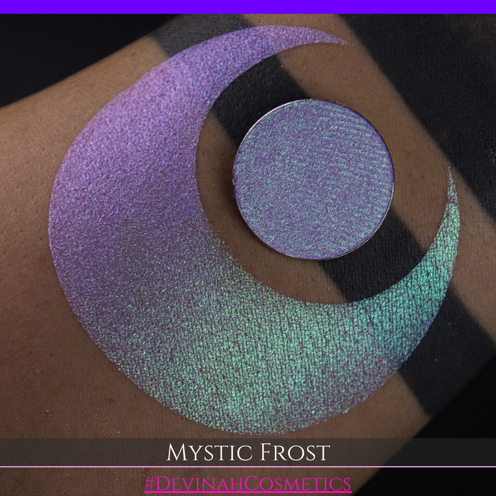A textured eyeshadow swatch labeled 'MYSTIC FROST' with a purple-to-teal gradient, showing a circular eyeshadow makeup pan on a black background hand made by Devinah Cosmetics.