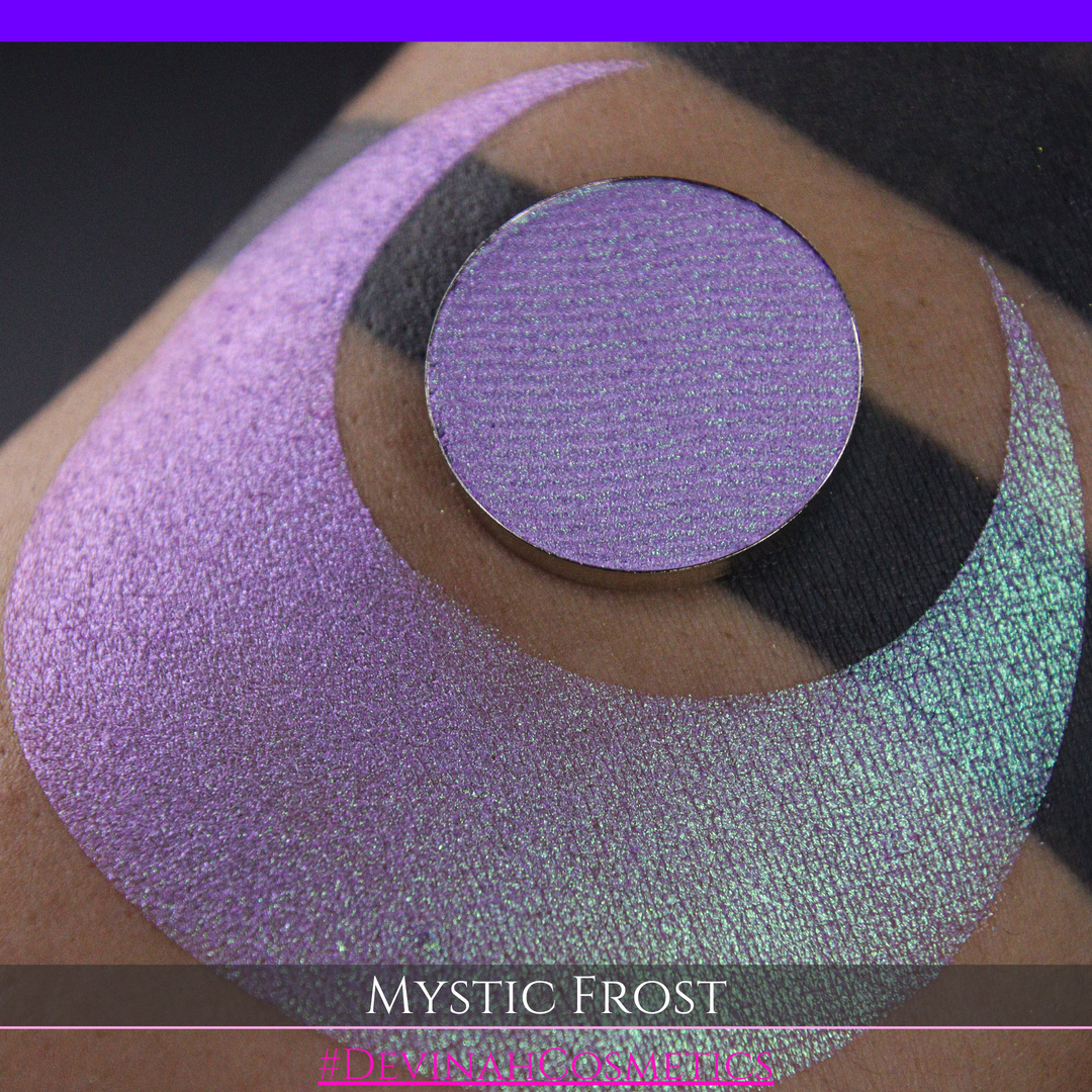 A textured eyeshadow swatch labeled 'MYSTIC FROST' with a purple-to-teal gradient, showing a circular eyeshadow makeup pan on a black background hand made by Devinah Cosmetics.