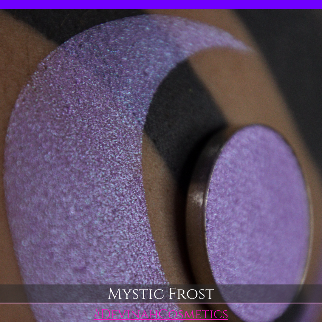 A textured eyeshadow swatch labeled 'MYSTIC FROST' with a purple-to-teal gradient, showing a circular eyeshadow makeup pan on a black background hand made by Devinah Cosmetics.