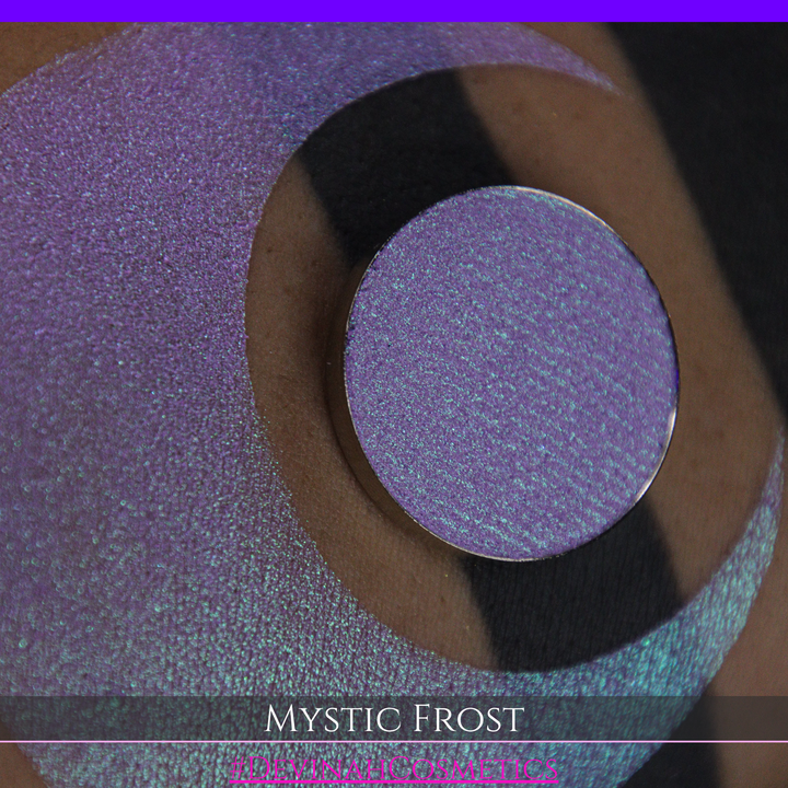 A textured eyeshadow swatch labeled 'MYSTIC FROST' with a purple-to-teal gradient, showing a circular eyeshadow makeup pan on a black background hand made by Devinah Cosmetics.