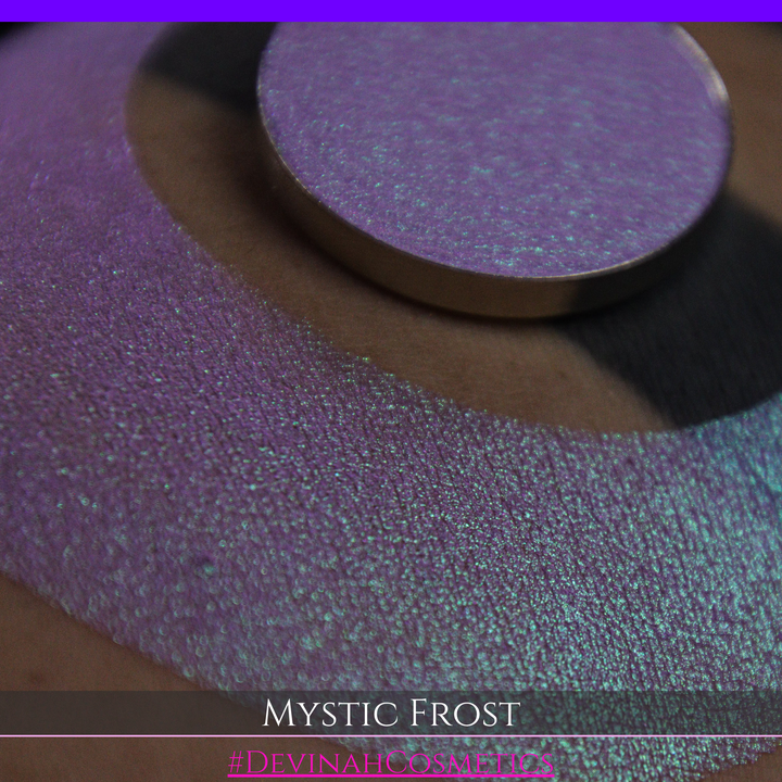 A textured eyeshadow swatch labeled 'MYSTIC FROST' with a purple-to-teal gradient, showing a circular eyeshadow makeup pan on a black background hand made by Devinah Cosmetics.