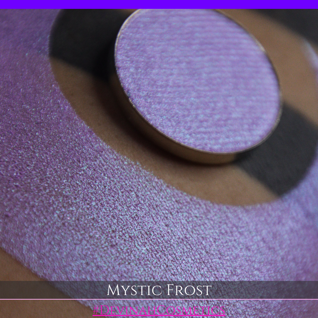 A textured eyeshadow swatch labeled 'MYSTIC FROST' with a purple-to-teal gradient, showing a circular eyeshadow makeup pan on a black background hand made by Devinah Cosmetics.