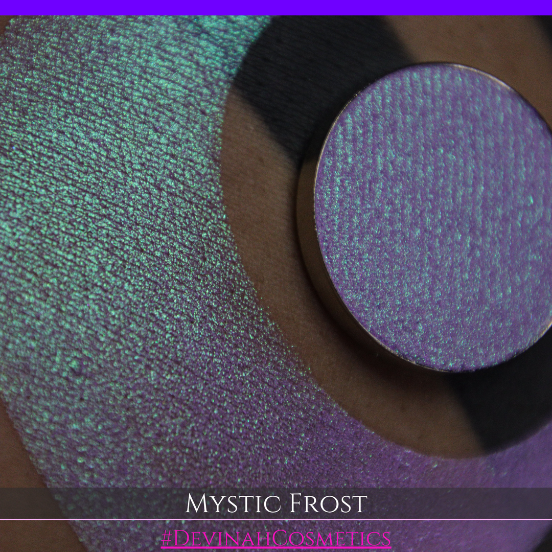 A textured eyeshadow swatch labeled 'MYSTIC FROST' with a purple-to-teal gradient, showing a circular eyeshadow makeup pan on a black background hand made by Devinah Cosmetics.
