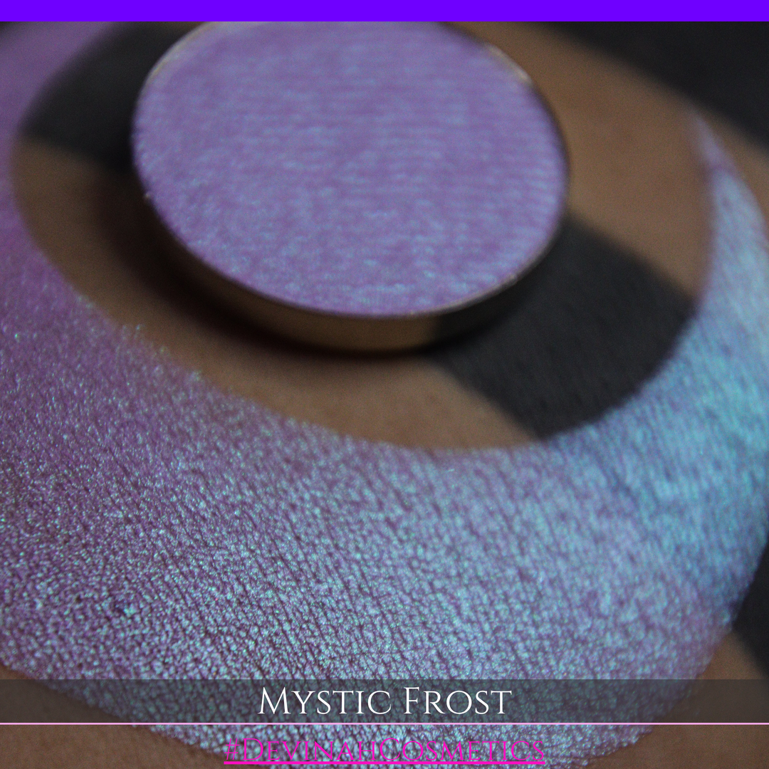 A textured eyeshadow swatch labeled 'MYSTIC FROST' with a purple-to-teal gradient, showing a circular eyeshadow makeup pan on a black background hand made by Devinah Cosmetics.