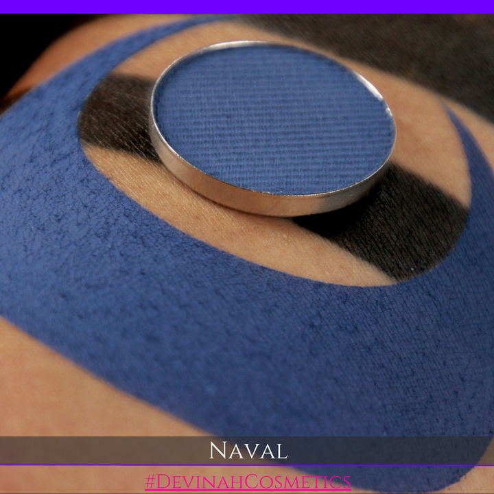 A close-up of a round makeup pan containing a deep navy blue pigment, placed on top of a blue and black patterned fabric. The text 'NAVAL' and '#DIVINAH COSMETICS' are displayed at the bottom.