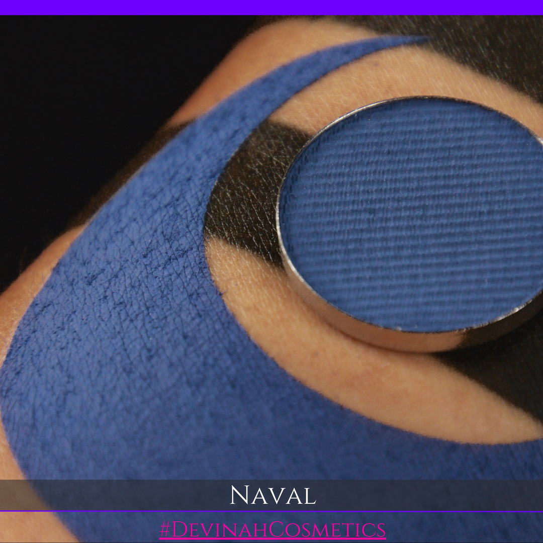 A close-up of a textured blue eyeshadow pan labeled 'NAVAL' by Devina Cosmetics, resting on skin with a matching blue eyeshadow applied in a circular shape.