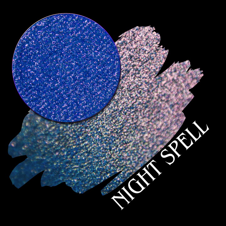 An eyeshadow swatch with a circular makeup eyeshadow pan with a blue and pink shift on a black background. The text 'NIGHT SPELL' appears diagonally in white by Devinah Cosmetics.
