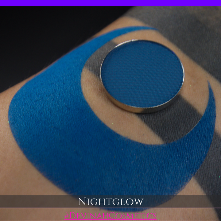 close up of a blue eyeshadow matte eyeshadow pan in  a deep blue color swatched on the skin in a crescent moon shape