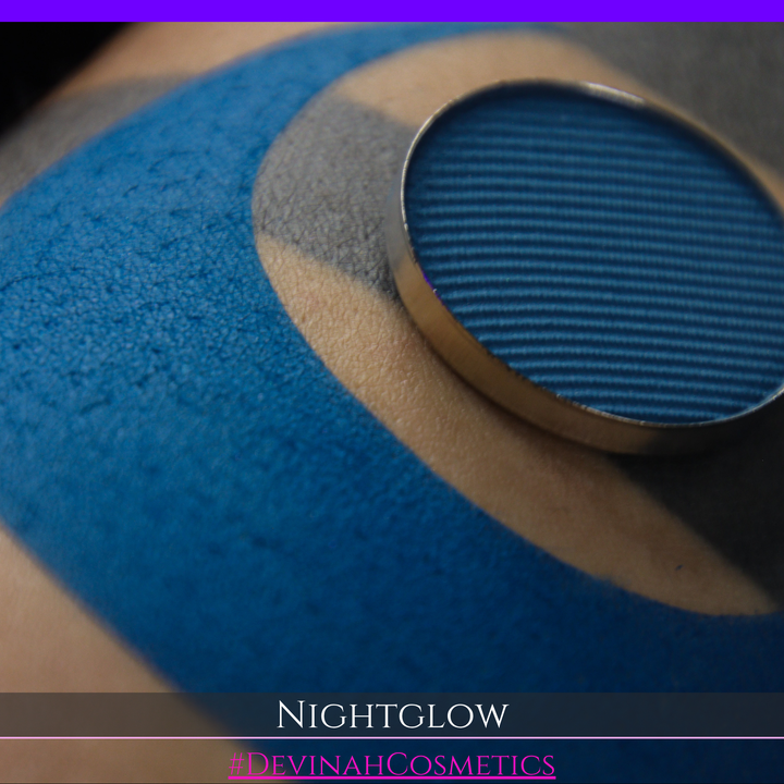 close up of a blue eyeshadow matte makeup pan with a blue swatch on tan skin