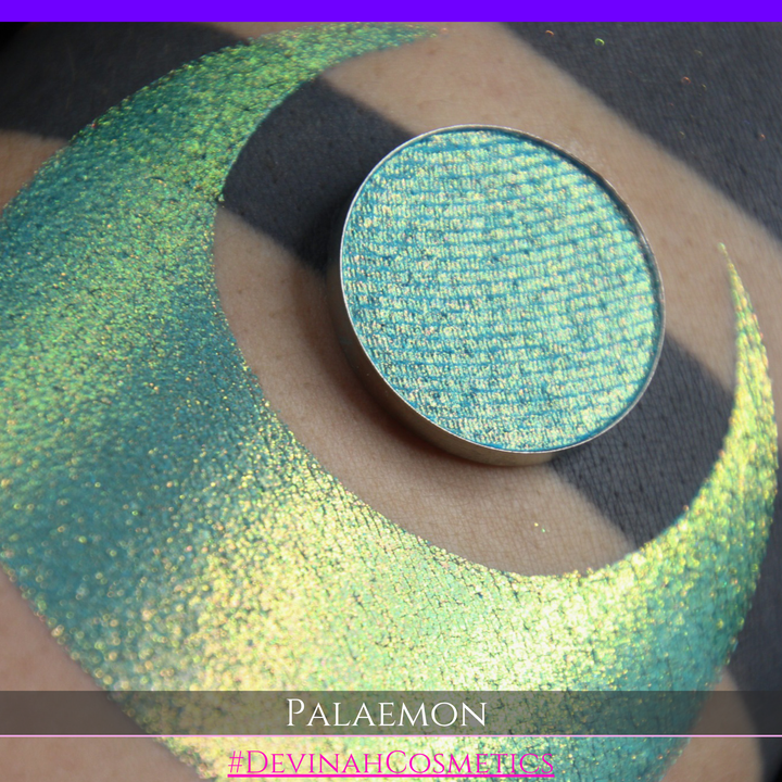 A round eyeshadow pan labeled 'PALAEMON' made by Devinah Cosmetics, placed over a large crescent moon swatch of the same shimmering shifty eyeshadow on skin. The eyeshadow has a duochrome multichrome shift between colors lime green, teal, yellow, gold, orange, pink, red.