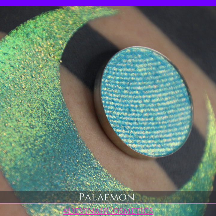 A round eyeshadow pan labeled 'PALAEMON' made by Devinah Cosmetics, placed over a large crescent moon swatch of the same shimmering shifty eyeshadow on skin. The eyeshadow has a duochrome multichrome shift between colors lime green, teal, yellow, gold, orange, pink, red.