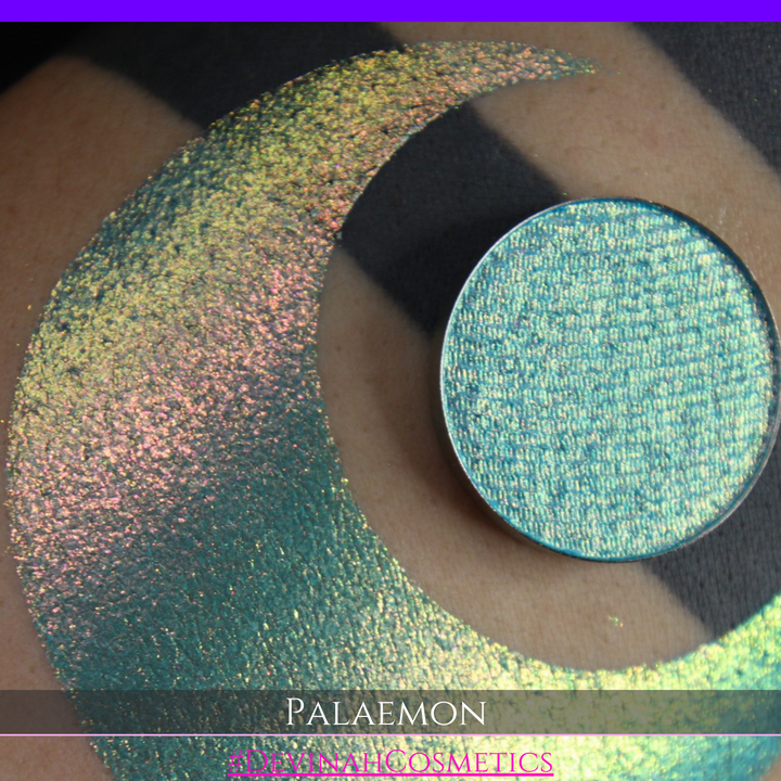 A round eyeshadow pan labeled 'PALAEMON' made by Devinah Cosmetics, placed over a large crescent moon swatch of the same shimmering shifty eyeshadow on skin. The eyeshadow has a duochrome multichrome shift between colors lime green, teal, yellow, gold, orange, pink, red.