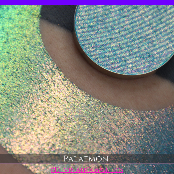 A round eyeshadow pan labeled 'PALAEMON' made by Devinah Cosmetics, placed over a large crescent moon swatch of the same shimmering shifty eyeshadow on skin. The eyeshadow has a duochrome multichrome shift between colors lime green, teal, yellow, gold, orange, pink, red.