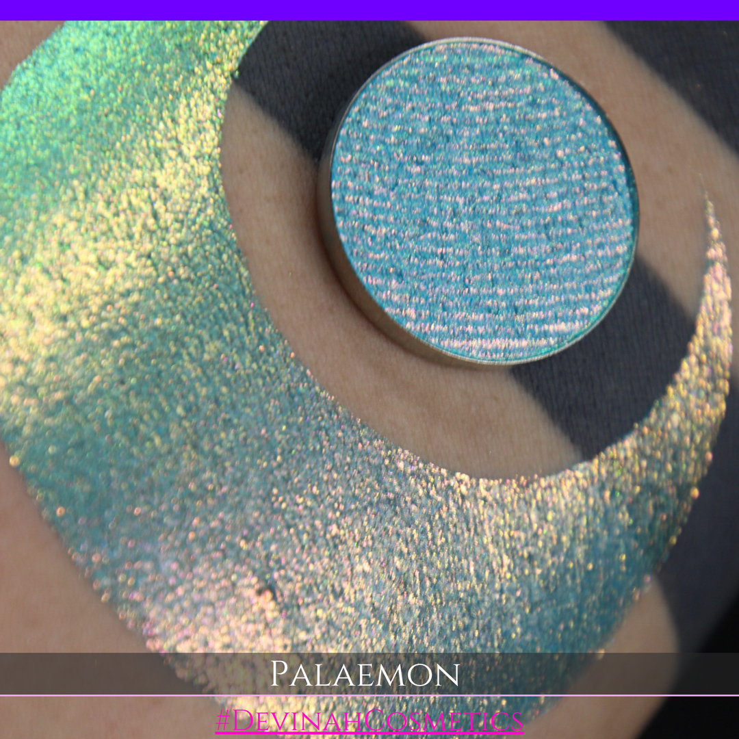 A round eyeshadow pan labeled 'PALAEMON' made by Devinah Cosmetics, placed over a large crescent moon swatch of the same shimmering shifty eyeshadow on skin. The eyeshadow has a duochrome multichrome shift between colors lime green, teal, yellow, gold, orange, pink, red.