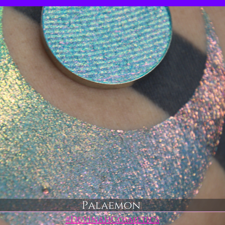 A round eyeshadow pan labeled 'PALAEMON' made by Devinah Cosmetics, placed over a large crescent moon swatch of the same shimmering shifty eyeshadow on skin. The eyeshadow has a duochrome multichrome shift between colors lime green, teal, yellow, gold, orange, pink, red.