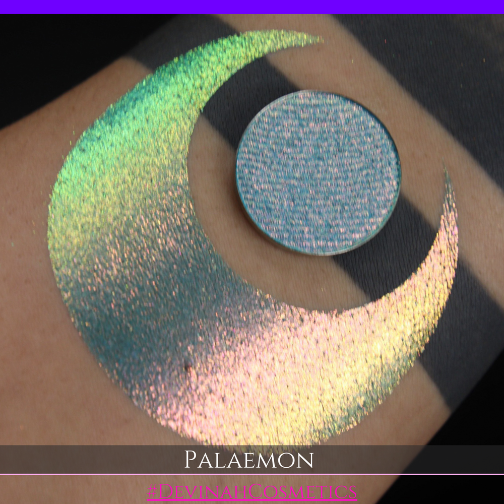 A round eyeshadow pan labeled 'PALAEMON' made by Devinah Cosmetics, placed over a large crescent moon swatch of the same shimmering shifty eyeshadow on skin. The eyeshadow has a duochrome multichrome shift between colors lime green, teal, yellow, gold, orange, pink, red.