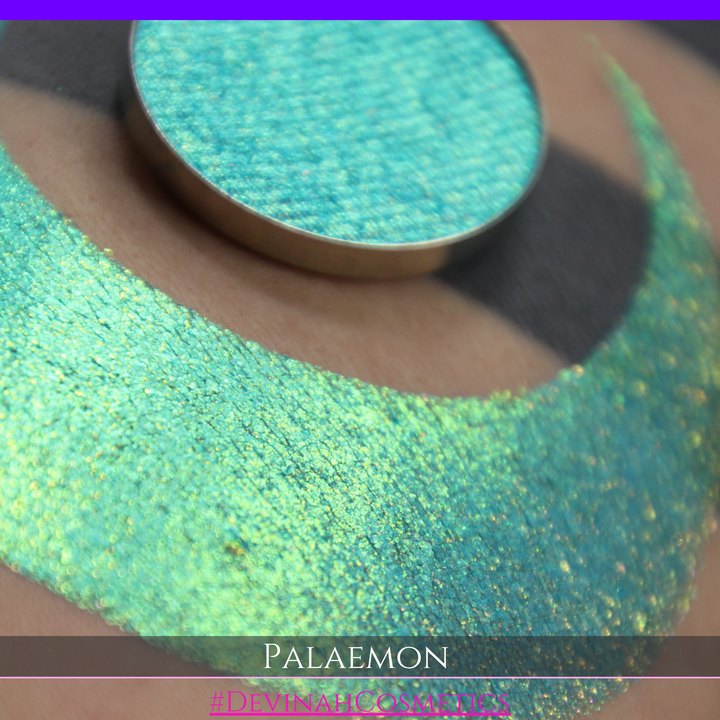 A round eyeshadow pan labeled 'PALAEMON' made by Devinah Cosmetics, placed over a large crescent moon swatch of the same shimmering shifty eyeshadow on skin. The eyeshadow has a duochrome multichrome shift between colors lime green, teal, yellow, gold, orange, pink, red.