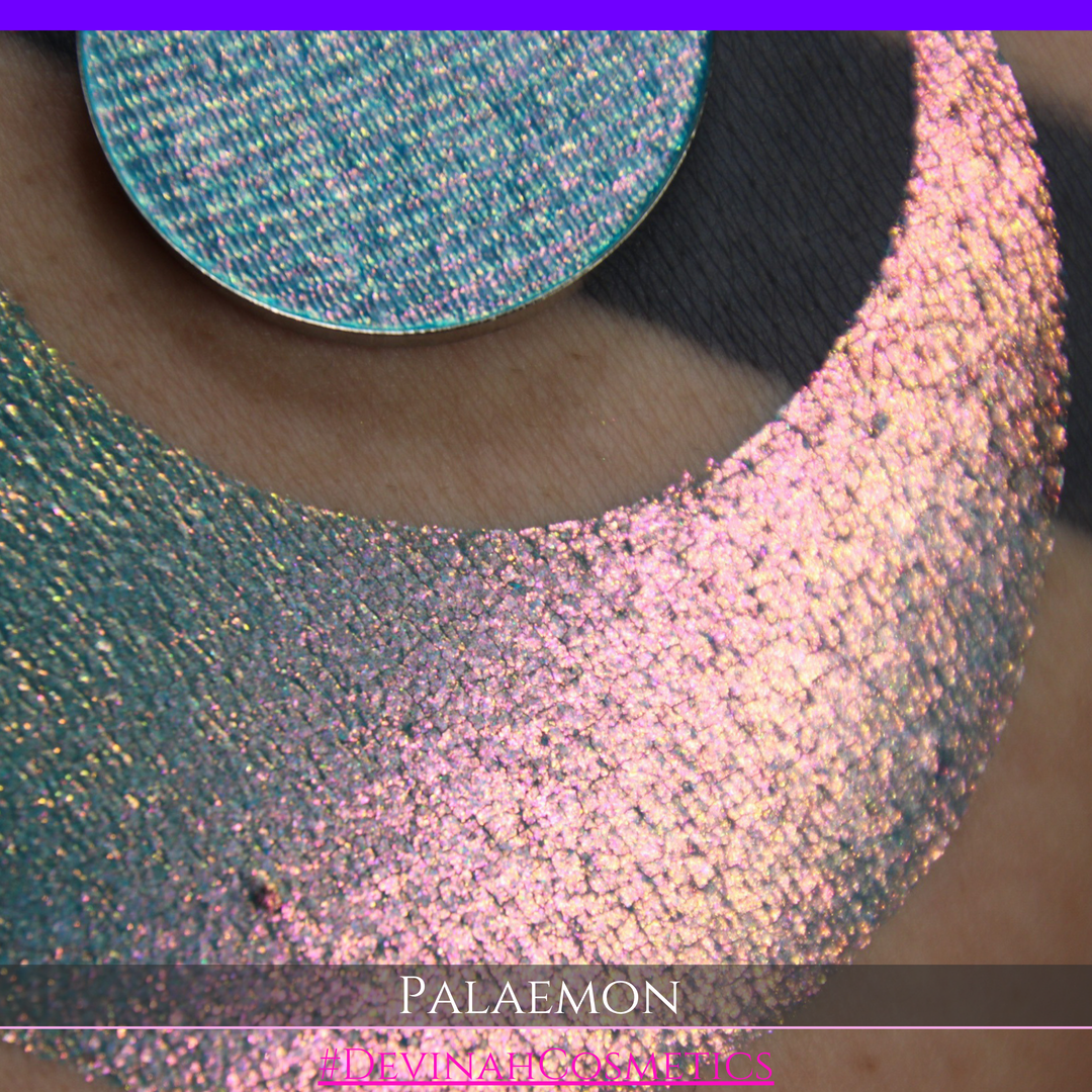 A round eyeshadow pan labeled 'PALAEMON' made by Devinah Cosmetics, placed over a large crescent moon swatch of the same shimmering shifty eyeshadow on skin. The eyeshadow has a duochrome multichrome shift between colors lime green, teal, yellow, gold, orange, pink, red.