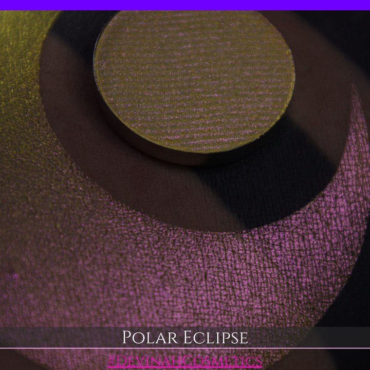 A close-up of a swatch and a circular  shimmering eyeshadow pan in a yellow-to-iridescent pink tone. Text at the bottom reads 'POLAR ECLIPSE' and '#DEVINAH Cosmetics'.