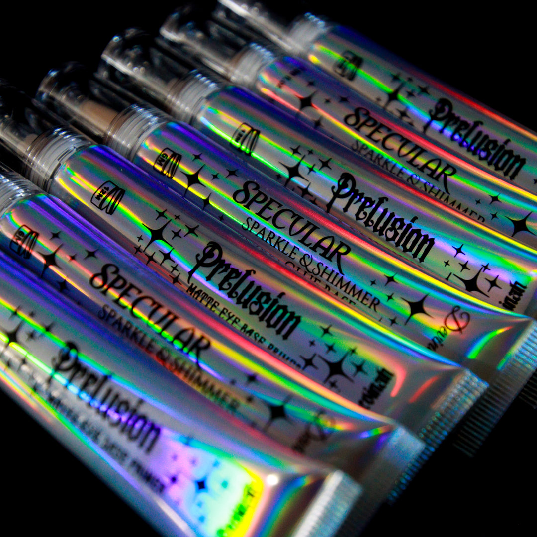 Several tubes of Precusion Matte Eye Base tube and Spectular Sparkle & Shimmer Glue Base tube arranged diagonally on a black background, showing a strong holographic rainbow sheen.