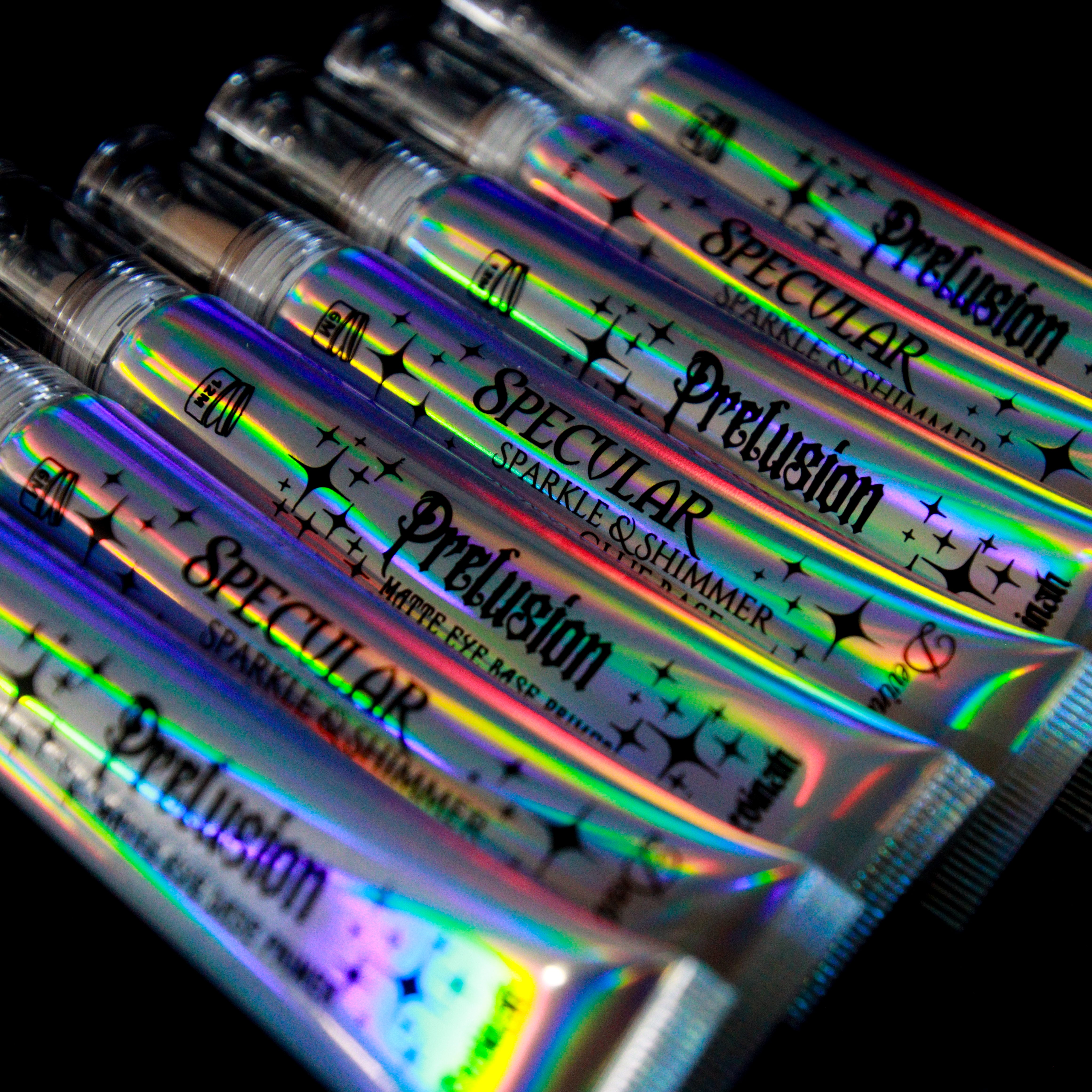 Several tubes of Precusion Matte Eye Base tube and Spectular Sparkle & Shimmer Glue Base tube arranged diagonally on a black background, showing a strong holographic rainbow sheen.