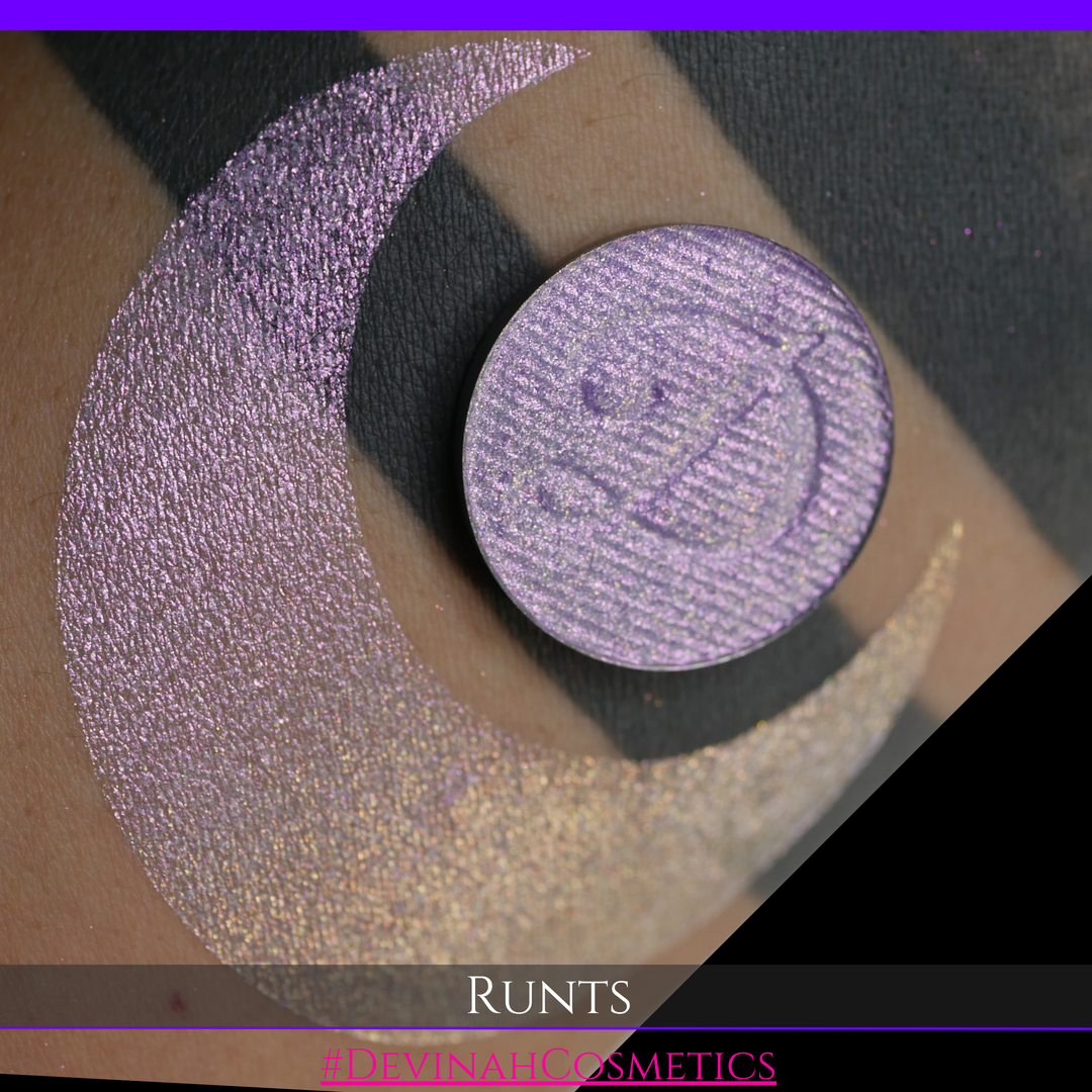 A round eyeshadow pan labeled 'RUNTS' made by Devinah Cosmetics, placed over a large crescent moon swatch of the same shimmering shifty eyeshadow on skin. The eyeshadow has a duochrome multichrome shift between colors purple pink and yellow