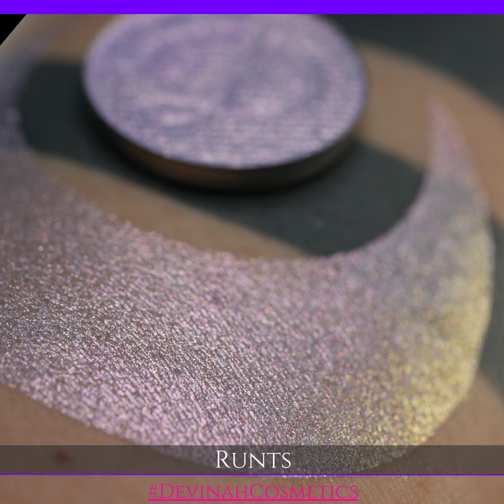 A round eyeshadow pan labeled 'RUNTS' made by Devinah Cosmetics, placed over a large crescent moon swatch of the same shimmering shifty eyeshadow on skin. The eyeshadow has a duochrome multichrome shift between colors purple pink and yellow