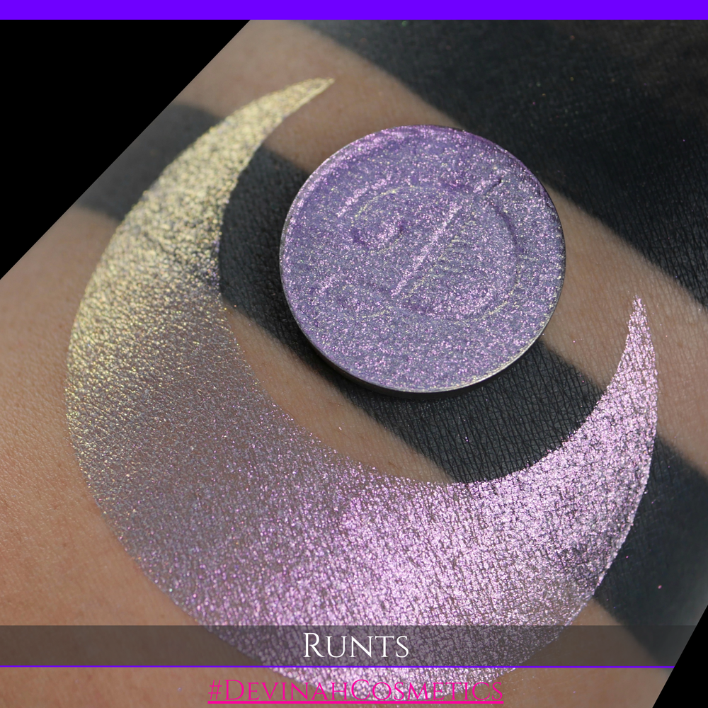 A round eyeshadow pan labeled 'RUNTS' made by Devinah Cosmetics, placed over a large crescent moon swatch of the same shimmering shifty eyeshadow on skin. The eyeshadow has a duochrome multichrome shift between colors purple pink and yellow
