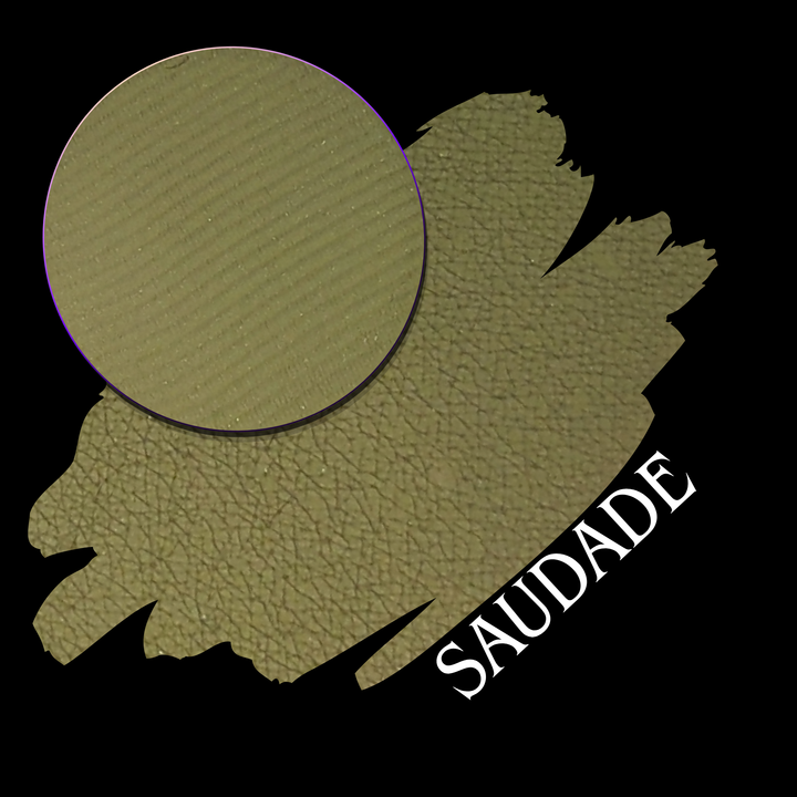 A textured olive green swatch with a circular makeup eyeshadow pan, labeled 'SAUDADE' on a black background.