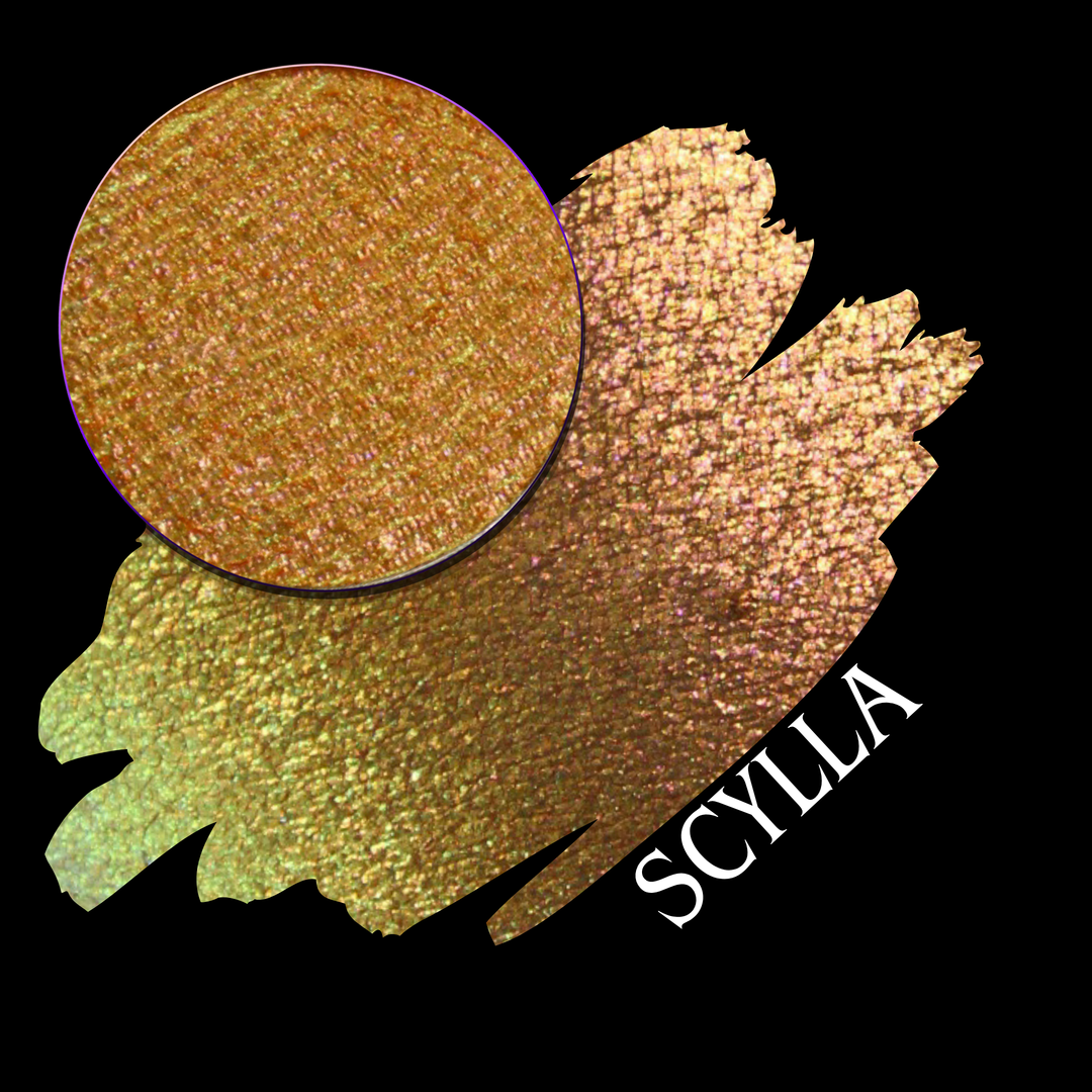 A round eyeshadow pan labeled 'SCYLLA' made by Devinah Cosmetics, placed over a large crescent moon swatch of the same shimmering shifty eyeshadow on skin. The eyeshadow has a duochrome multichrome shift between colors lime green, teal, yellow, gold, orange, pink, red.