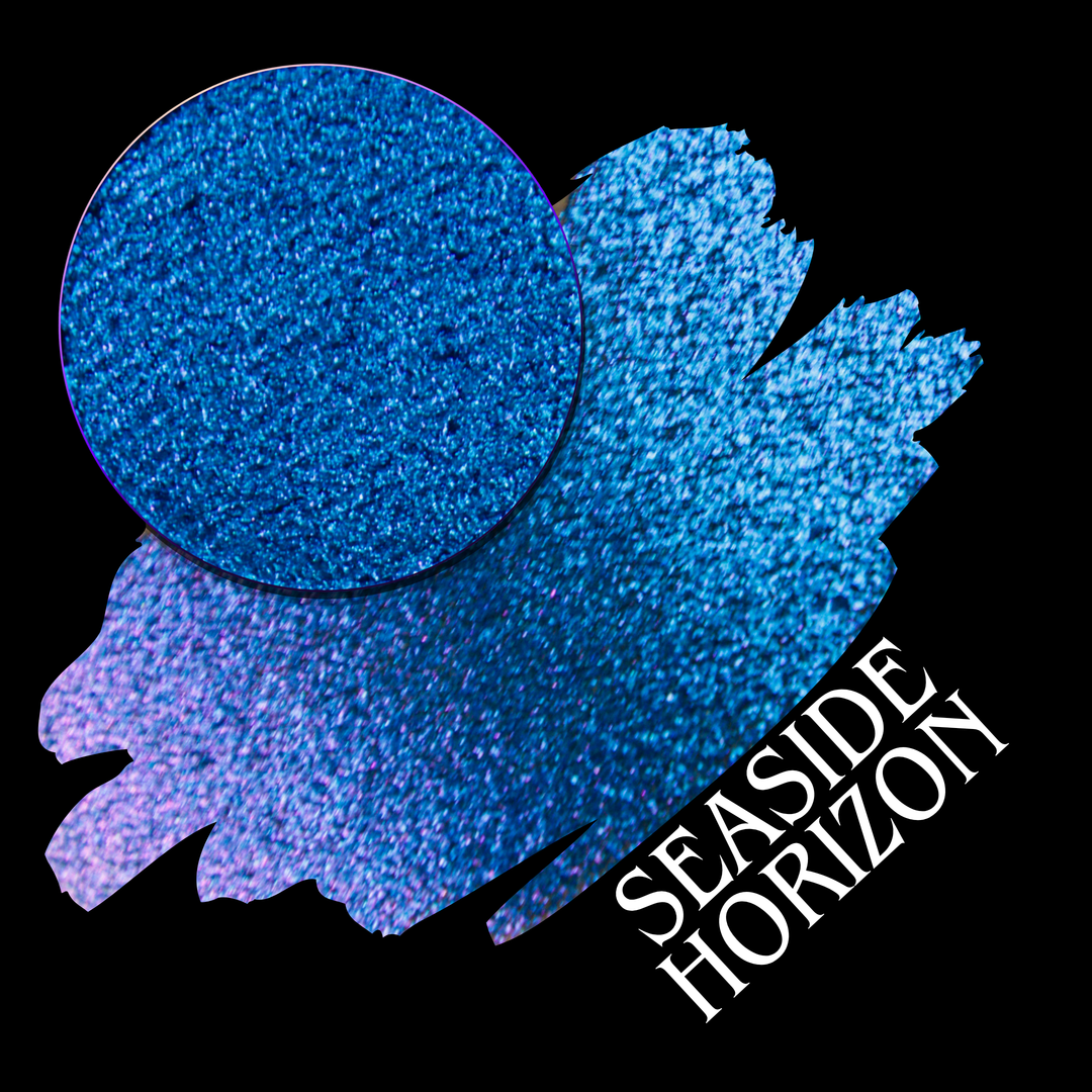 A round eyeshadow pan labeled 'SEASIDE HORIZON' made by Devinah Cosmetics, placed over a large crescent moon swatch of the same shimmering shifty eyeshadow on skin. The eyeshadow has a shift between colors purple, blue.