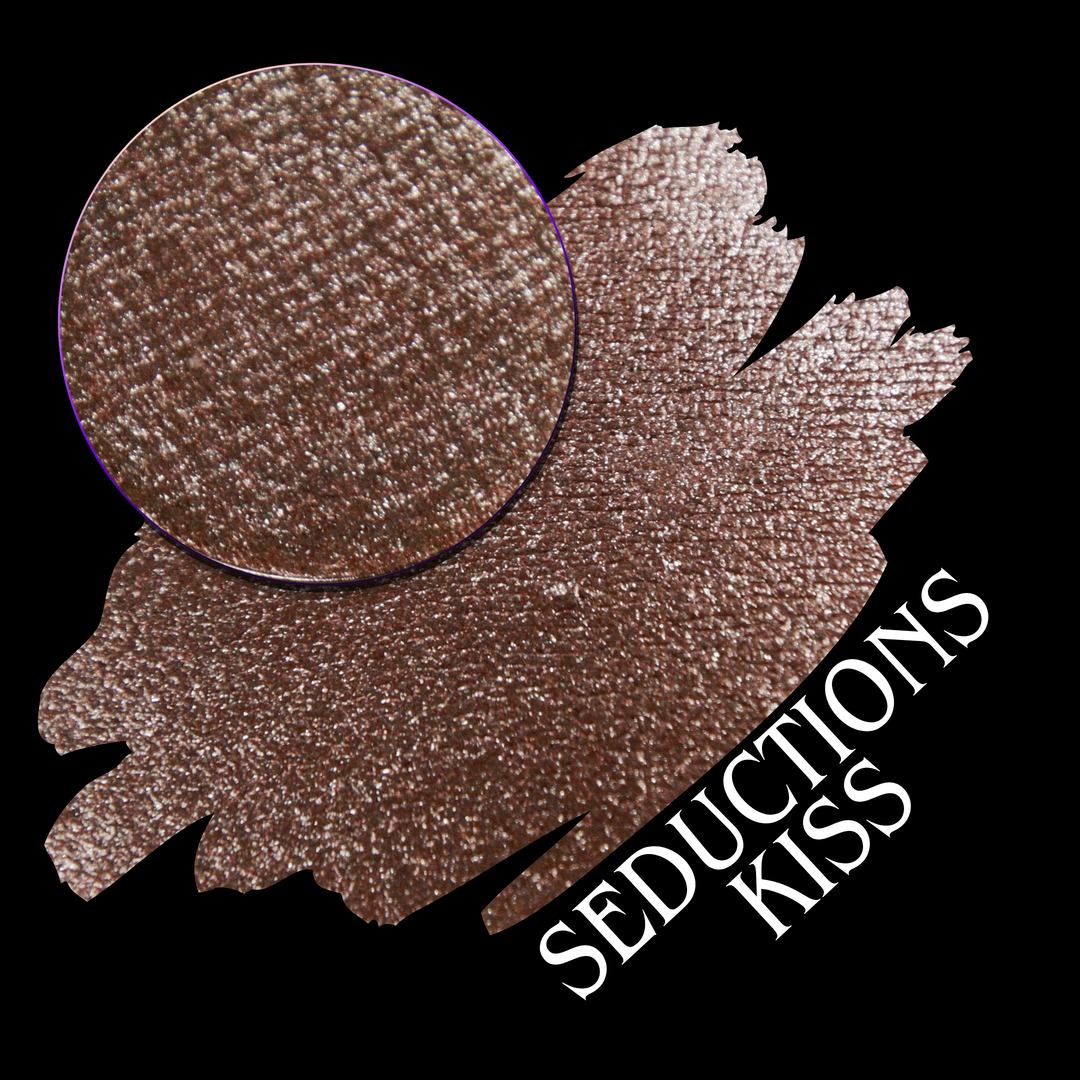 A round eyeshadow pan labeled 'SEDUCTIONS KISS' made by Devinah Cosmetics, placed over a large crescent moon swatch of the same shimmering shifty eyeshadow on skin. The eyeshadow has colors brown, tan, creme sparkle shimmer.