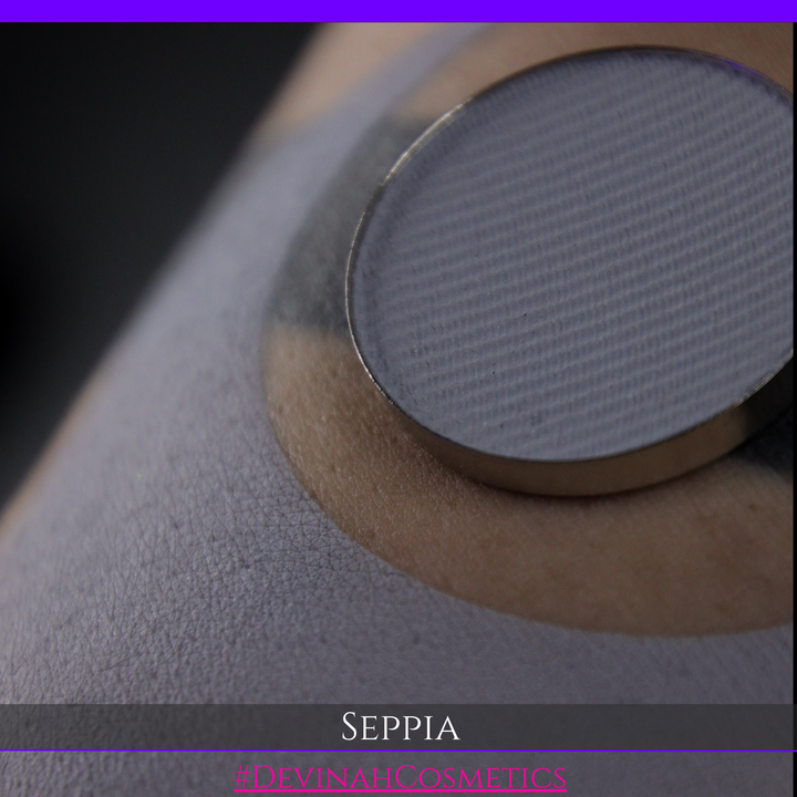 A close-up of a circular makeup eyeshadow matte pigment pan of 'Seppia' eyeshadow with a swatch of the matte eyeshadow. The brand name 'DEVINAH COSMETICS' is visible at the bottom